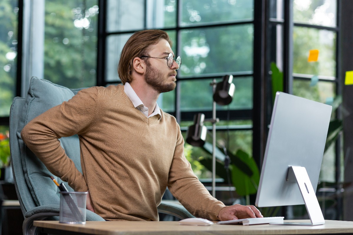 Man in office massaging back and contemplating ergonomic tips for dedicated desk setups