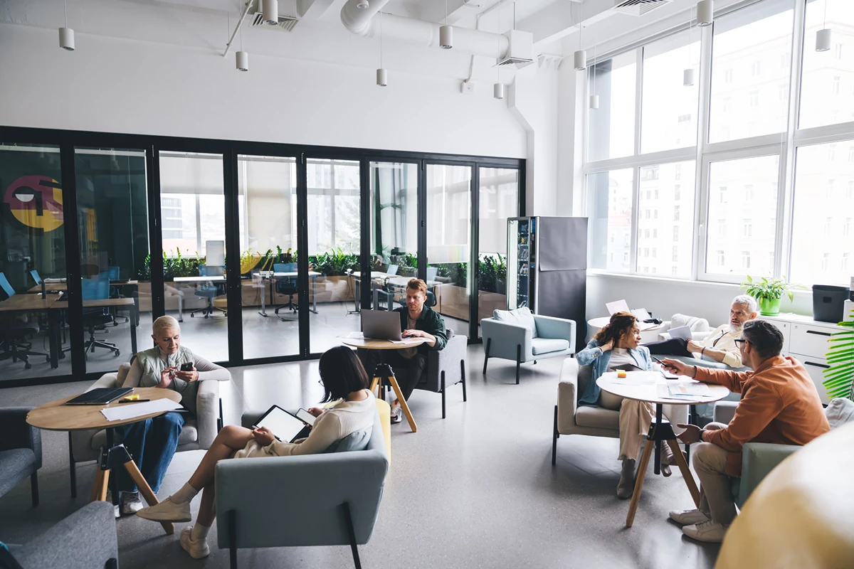Coworkers having discussions in a coworking space with a private office in the background.