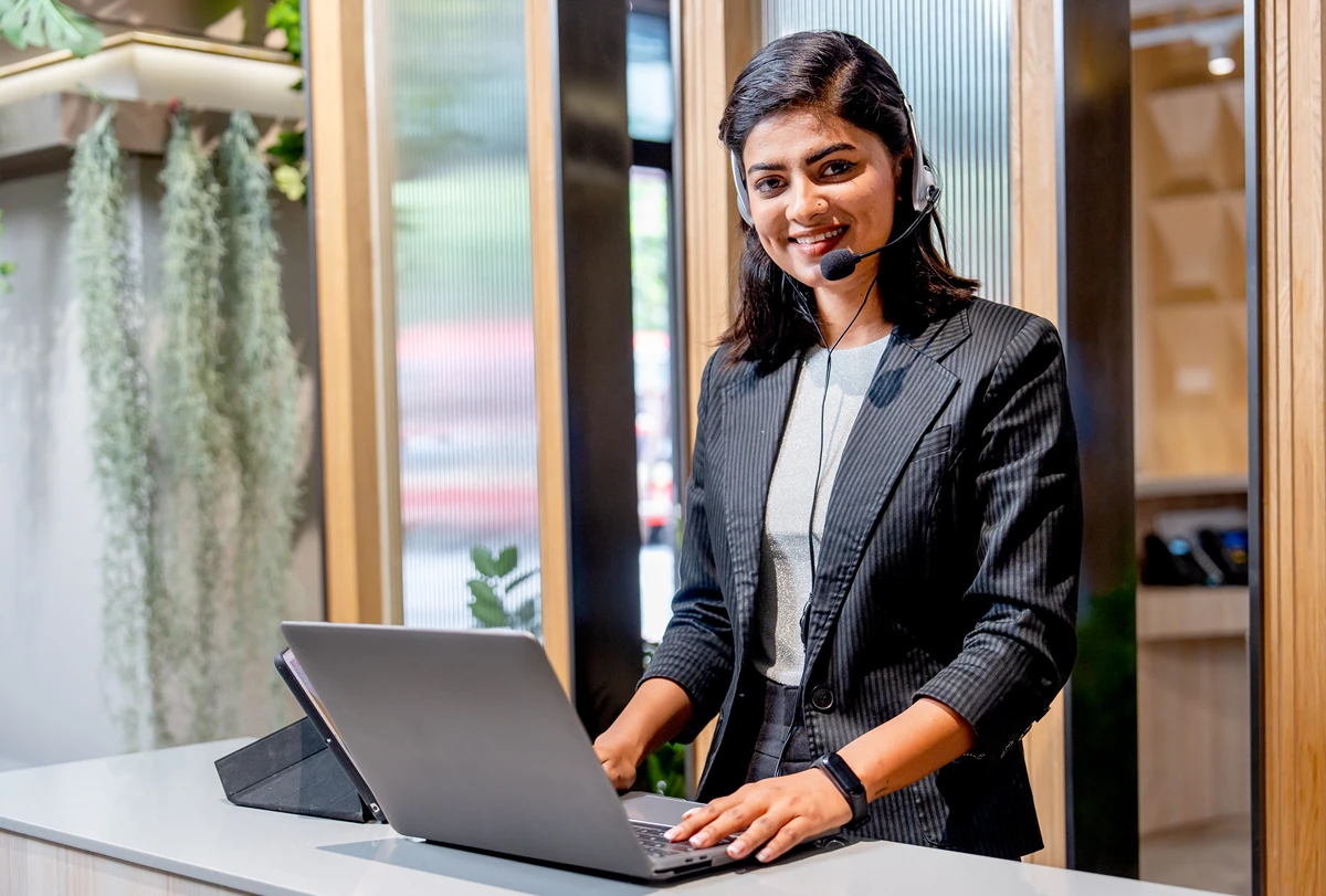 A virtual receptionist wearing a headset, using a laptop